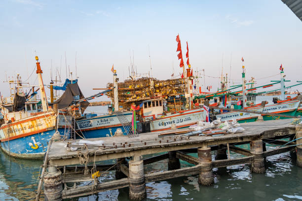 fishing boats of traditional design add pops of color to the picturesque harbor of thailand, as they rest at the pier. - harbor editorial industrial ship container ship imagens e fotografias de stock