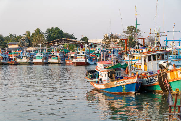 fishing boats of traditional design add pops of color to the picturesque harbor of thailand, as they rest at the pier. - harbor editorial industrial ship container ship imagens e fotografias de stock