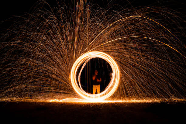istock Spinning and burning Steel wool sparkle fire in the circle shape with long speed shutter shoot glowing light line to the ground. 1467816779