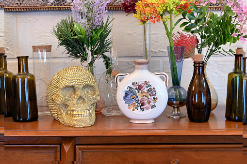 Golden skull on table with beautiful bottle and flowers in vase