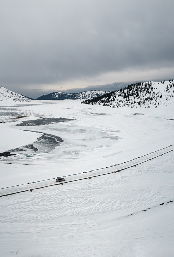 Aerial drone photography of a snowy mountain with a car on the road. Winter landscape with the frozen Belmeken dam in Rila Mountains.