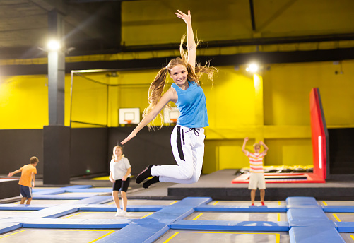 Cheerful active teen girl enjoying jumping on trampoline on indoor inflatable playground
