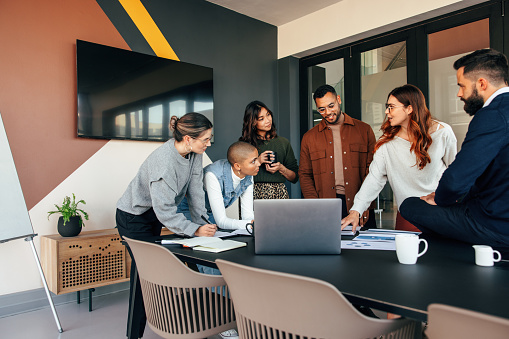 Diverse businesspeople discussing some reports in a boardroom. Group of multicultural businesspeople standing around a table in a modern office. Young entrepreneurs collaborating on a project.