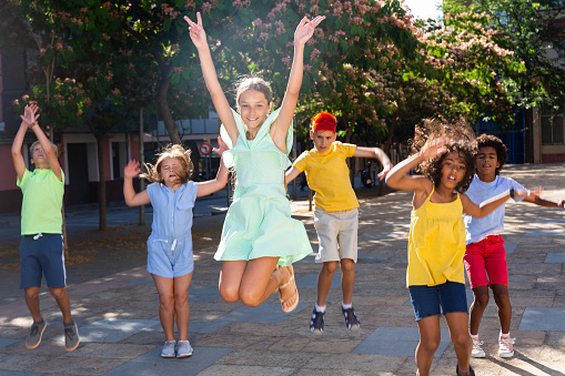 Happy multiracial boys and girls jumping outdoors during summer day.