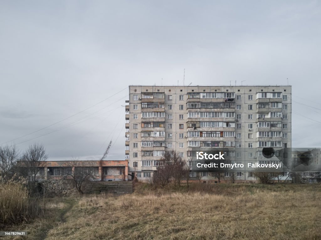 Gloomy cloudy cityscape with old gray concrete soviet prefabricated nine-storey panel apartment building. Former Soviet Union Stock Photo