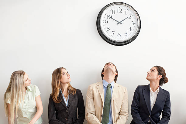 Four Businesspeople Watching Clock Four businesspeople sitting on bench and looking up at clock. Horizontally framed shot. impatient stock pictures, royalty-free photos & images