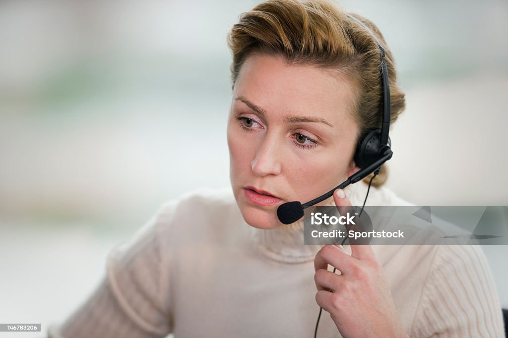 Woman touching headset and staring in front of her Young professional female wearing headset. Customer Service Representative Stock Photo