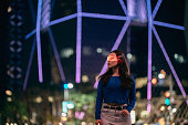 Young asian woman using smart glasses standing in front of glowing modern building at night