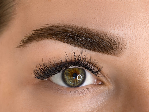 Making makeup in a beauty salon. Applying black mascara to the eyelashes with a makeup brush. Close-up of a woman's eye. Lengthening of the eyelashes after lamination.