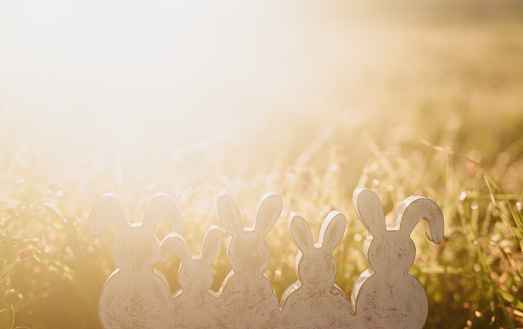 Five white and grey vintage painted easter rabbits figurines sitting in the meadow with extremely romantic backlight. Selective and soft focus. Part of a series.