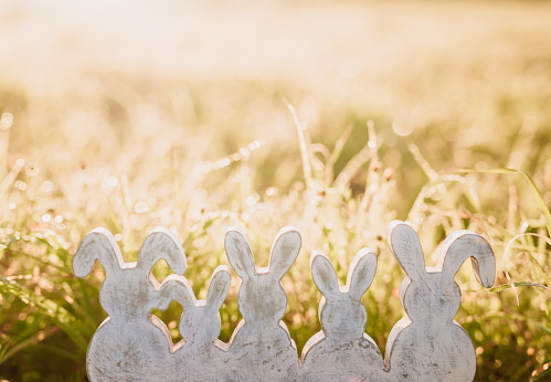 Five vintage painted easter rabbits figurines sitting in the meadow with romantic backlight. Selective and soft focus. Part of a series.