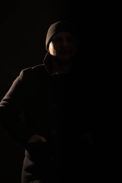 istock Man with coat and hat hiding in shadow and silhouette illuminate with light 1467837693