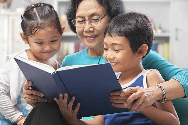 a avó e netos a ler um livro juntos - grandparent reading grandmother child imagens e fotografias de stock