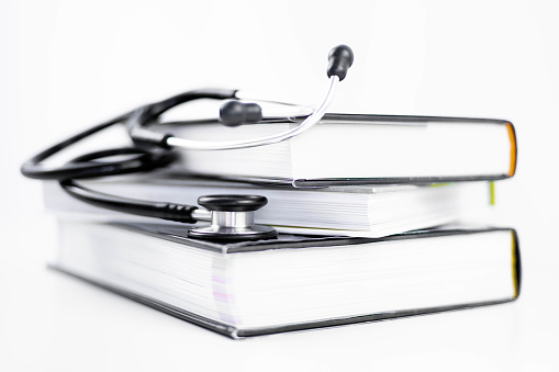 Side view of a stethoscope listening to stacked medicine books on a white background with copy space. Isolated concept of learning and studying medicine, cardiology and health. University and hospital.