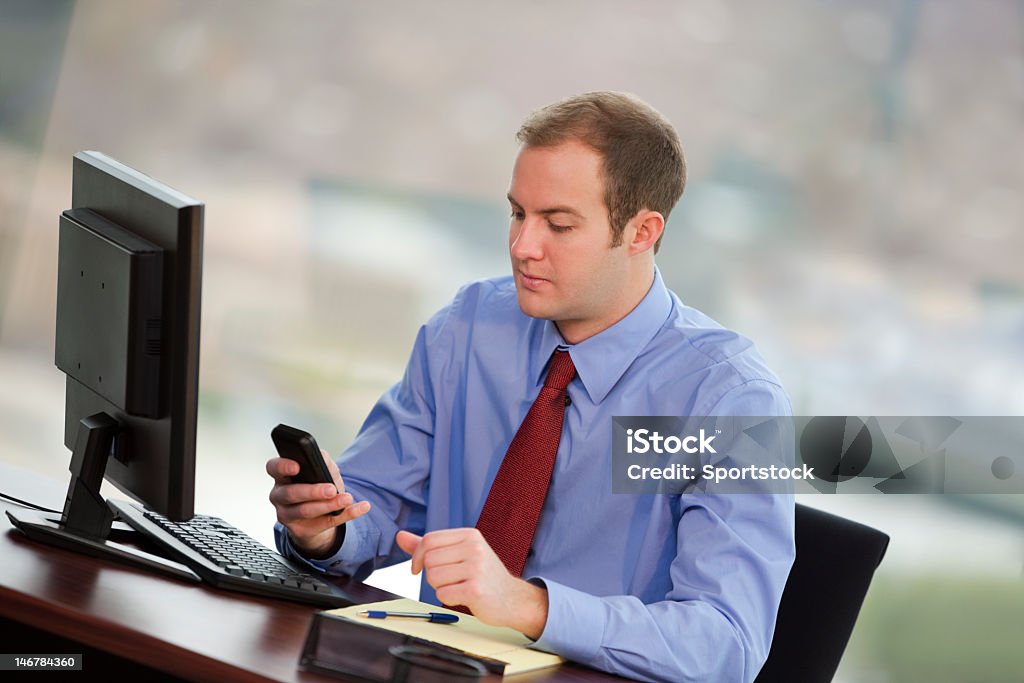 Uomo d'affari In ufficio guardando cellulare - Foto stock royalty-free di Close-up
