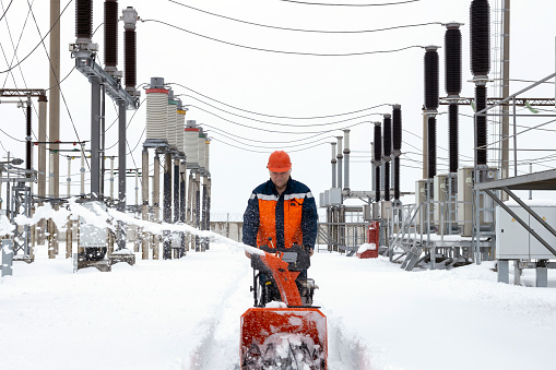 A man works with a snow blower to remove freshly fallen snow from a driveway after a storm. At the power station.