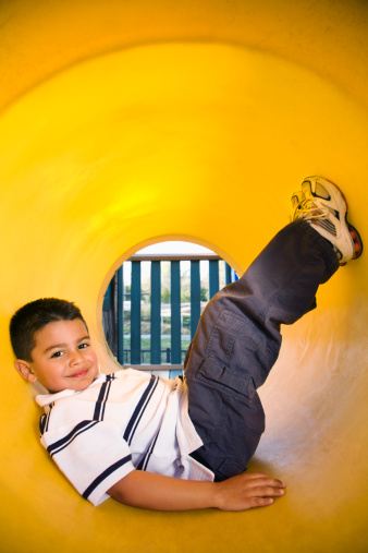 Young boy lying in crawl tube at playground. Vertically framed shot.