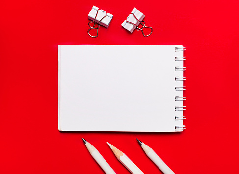 White notepad with space to insert text, white pencils and paper clips on a bright red background