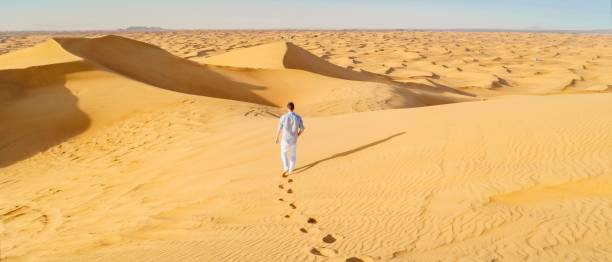 junge männer zu fuß in der wüste von dubai, sanddünen von dubai vereinigte arabische emirate - dubai united arab emirates traditional culture camel stock-fotos und bilder