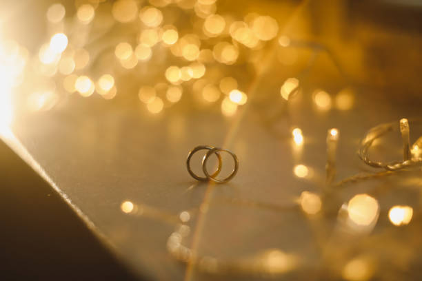 anéis de casamento em bokeh borrado fundo dourado brilhante. símbolo de amor e romance em um fundo de glitter texturizado com espaço de cópia para sua saudação ou parabéns - 13414 - fotografias e filmes do acervo