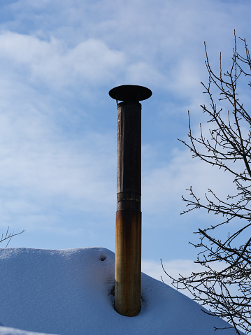 An old metal chimney on a snow-covered roof against blue sky background. Winter time.