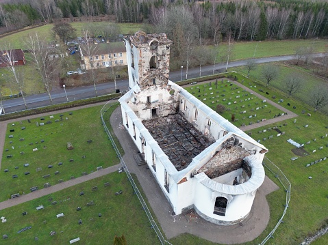 Aerial view of an ancient chapel in ruins, surrounded by lush green grass and a cemetery of tombstones