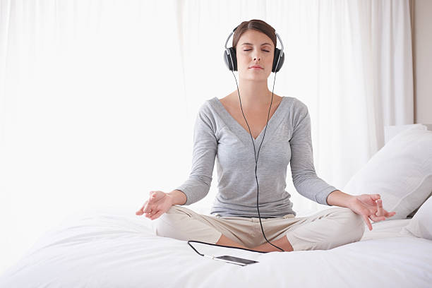 女性、ヘッドフォン上のベッドで座禅 - lotus position audio ストックフォトと画像