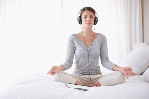 Young woman with headphones sitting in lotus position on bed by copyspace