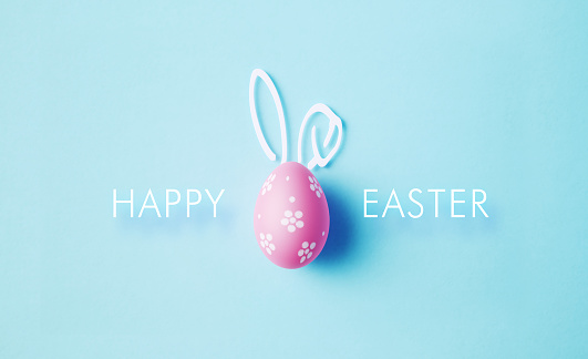 Painted pink Easter egg with bunny ears and happy Easter message on blue background. Horizontal composition with copy space. Easter concept.