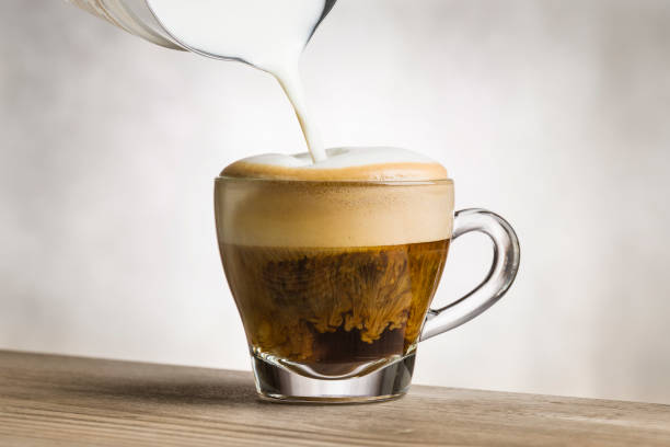 Cappuccino on wooden table Making cappuccino in glass cup with milk frother on wooden table. cafe transparent glass table stock pictures, royalty-free photos & images