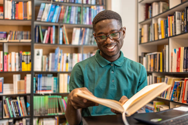 istock Smiling African American student enjoying book reading in library 1467863844