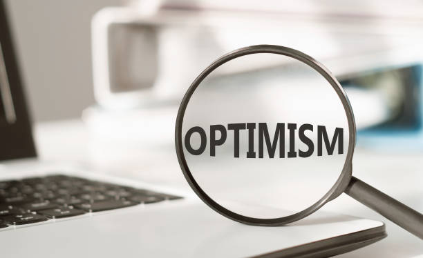 istock Optimism word under magnifying glass lying on a laptop on white office background. Business and optimism or pessimism concept. 1467864389