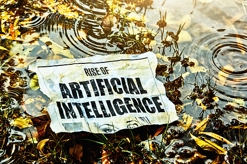 Cut-out newspaper headline about the Rise of Artificial Intelligence, lying discarded in a marsh in the rain.