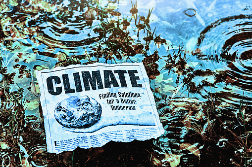 Cutting of simulated newspaper article about climate change outdoors in rainy weather in a swampy area. Text was written by the photographer, who also did the design and took the photo of the hand. Public domain satellite image from https://www.nasa.gov/multimedia/imagegallery/image_feature_2159.html