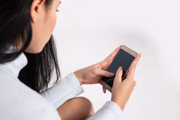 istock Pretty young asian woman using smartphone standing on isolated white background. She texting on cell phone. 1467865600