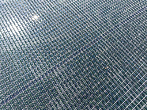 Greenhouse for growing vegetables on an industrial scale aerial view from above with clouds reflected in the glass.