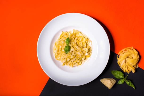istock Pasta with cheese, basil and white sauce in a plate on a yellow-black background with scattered foods 1467870774