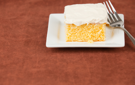 piece of yellow cake on small white plate over brown fabric