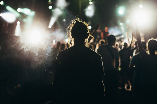 Silhouette of a young man having fun while listening music performance in a concert crowd on a music festival. Nightlife and music entertainment concept.