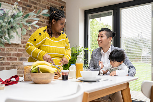 Waist-up view of early 30s Asian man and multiracial woman conversing as they do healthy morning meal routine with their toddler son.