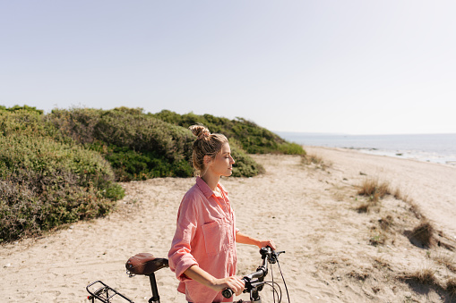 Photo of a young woman, exploring the coastline and enjoy beautiful summer morning on a bicycle