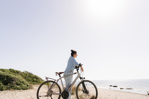 Photo of a young woman, exploring the coastline and enjoy beautiful summer morning on a bicycle
