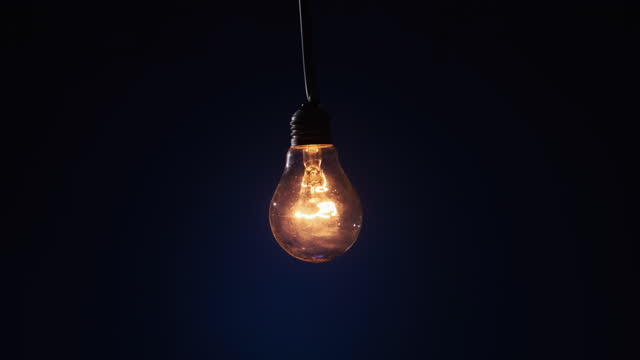 Incandescent Lamp on Wire Glows and Flickers on Dark Blue Background