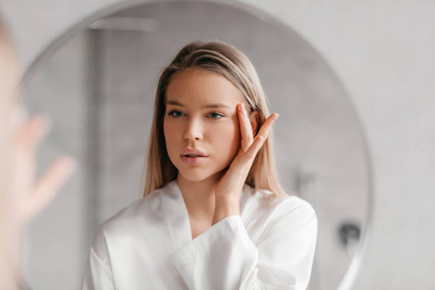 istock Pretty young woman looking at mirror and touching face while doing morning beauty routine in bathroom 1467885578