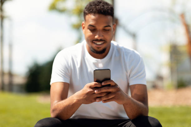 istock Mobile communication concept. Happy black guy using smartphone outdoors, sitting in parkland, selective focus 1467886285