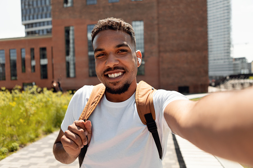 Photography Concept. Portrait of smiling young black man taking selfie picture, point of view pov shot of happy male looking at the camera making front selfportrait outdoors, holding using cellphone