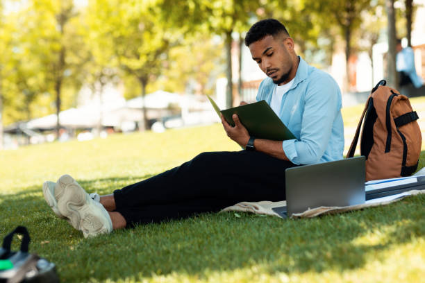 istock E-learning concept. African american male student preparing for lecture, using laptop and taking notes, sitting in park 1467886743