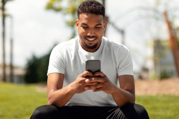 istock Smiling african american guy chatting on smartphone, texting in social media while sitting in park outdoors, copy space 1467886754