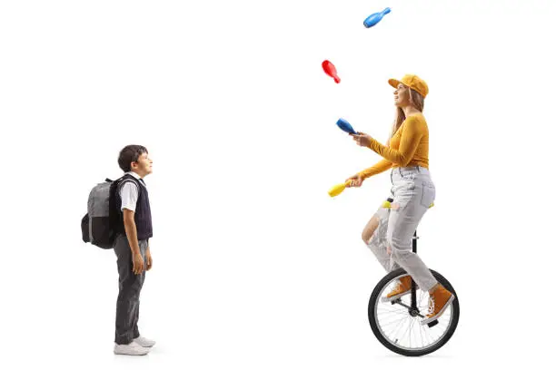 Boy standing and watching a female riding a mono cycle and juggling isolated on white background