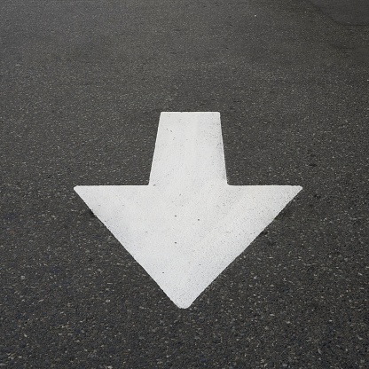 White traffic arrow on the grey asphalt directs vehicles to drive in a straight direction.
